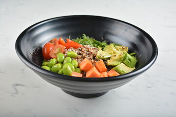 trio quinoa grain salad bowl with avocado, tomato, pea bean, carrot and brown rice in black bowl in white marble healthy poke bowl menu