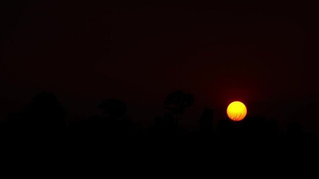 4K Silhouette concept with orange sun slowly setting against dark sky. 