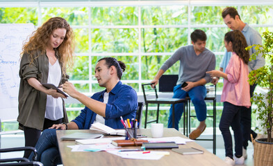 Focus handsome Caucasian male boss teaching, explaining, giving advice to hipster trendy creative female subordinate in comfortable modern office with profession and background of diverse staff.