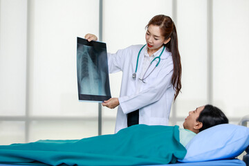 Obraz premium Young Asian female doctor demonstrating x ray scan to patient lying on bed while explaining medical treatment in modern hospital