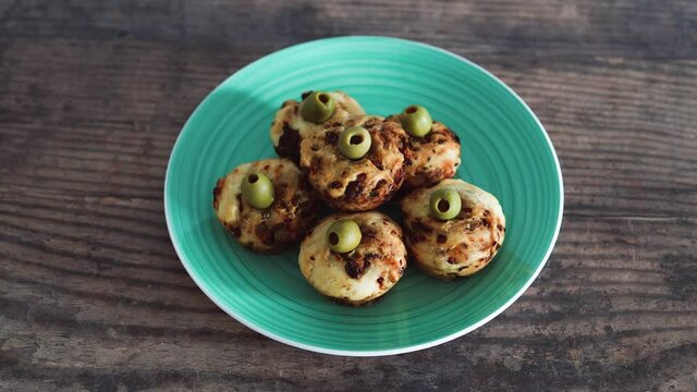 vegan focaccia savory muffins with sundried tomatoes and olives served on a green plate, healthy plant-based food