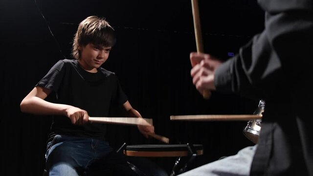 Young caucasian woman teaches a boy to play the drums in the studio on a black background. Music school student