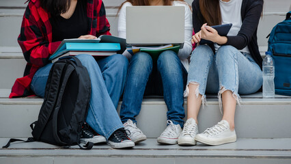 Group of three young girls college students legs and sneakers sitting together in university campus...