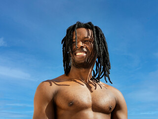 Handsome man smiling under the sun at the beach, blue sky 