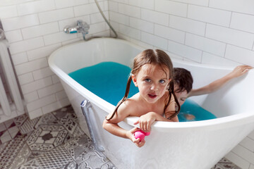 From above of adorable little brother and sister bathing in bathtub with blue water and having fun...