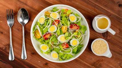 Big white bowl of lettuce, sprout salad with boil egg, onion and tomato mix with Japanese sesame oil dressing on wooden table together with small olive oil jar and sesame cup and utensil beside