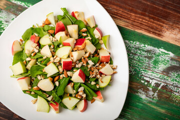 Healthy vegetarian rocket salad with dices apple, and chop almond in white dish place on colourful wooded table.  Concept for healthy