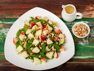 Healthy vegetarian rocket salad with dices apple, and chop almond in white dish place on colourful wooded table.  Concept for healthy