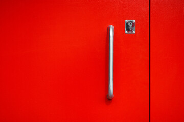 Steel door handle with lock and bright red metal front door, outside. Painted metal texture....