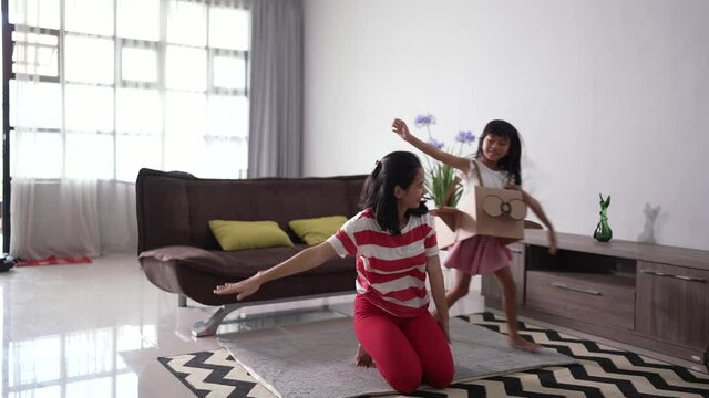 asian little girl playing with cardboard toy airplane at home with her mother