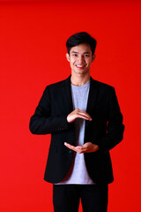 Obraz na płótnie Canvas Asian young man smart and handsome standing look at camera with smile on face.Posing in hand holding something Shoot in studio with red background and copy space to be design advertising banner