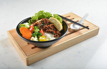 asian spicy thai basil minced pork rice bowl with fried vegetable salad in black bowl in white...