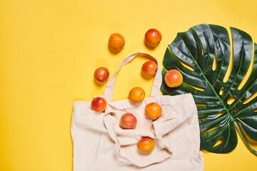 Peaches are lying on a white bag with handles and on a palm leaf