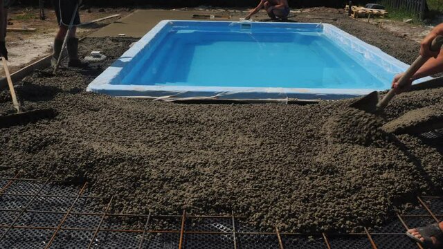 A team of builders levels the concrete around the pool. Construction of a hotel with a swimming pool
