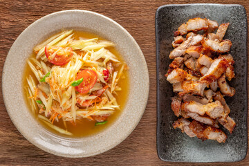 Som Tum Thai, Som Tam Thai, Thai food, spicy papaya salad and fried pork in ceramic plate on rustic natural wood texture background, top view
