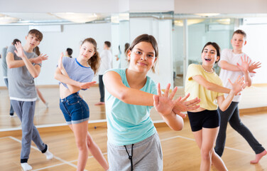Fototapeta premium Portrait of emotional teenager girl doing dance workout during group class in studio