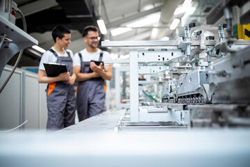 Production line workers controlling manufacturing process of modern packaging industrial machine in...