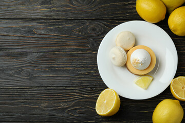 Plate with cupcake and macaroons, and lemons on wooden table