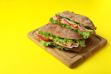 Board with ciabatta sandwiches on yellow background
