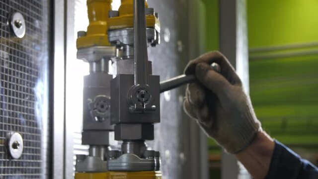 Employee hand in dirty glove turns metal lever on pipe with flanges near production line at plant extreme closeup
