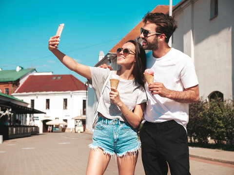 Smiling beautiful woman and her handsome boyfriend. Woman in casual summer clothes. Happy cheerful family. Couple posing in the street. Eating tasty ice cream in waffles cone. Taking selfie photos