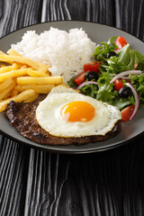 Bitoque is a classic Portuguese dish that is simply a steak drizzled with a butter pan sauce and topped with a fried egg closeup in the plate on the table. Vertical