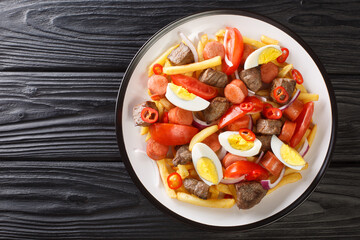 Pique macho is a Bolivian dish consisting of a layer of french fries buried underneath a heap of chopped beef, sausages, eggs, tomato, onions, peppers closeup in the plate. Horizontal top view - obrazy, fototapety, plakaty