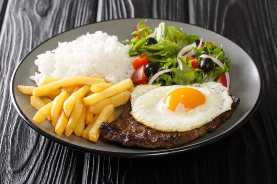 Bitoque Is A Beloved Portuguese Dish That Includes Lean Steak Accompanied By Rice And French Fries Topped With A Fried Egg Closeup In The Plate On The Table. Horizontal