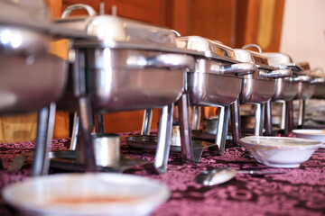 Close up of stainless steel food containers on table at wedding party. Catering service. No people. Selective focus. Perspective view