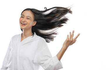 smiling asian girl wearing a towel is standing with her long black hair blowing by wind on gray...