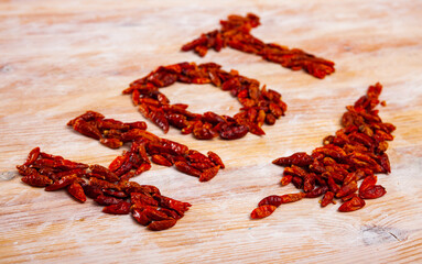 Word HOT lined with small dried spicy cayenne peppers on wooden background