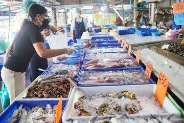 woman's hand putting on plastic glove and holding serving 
 tongs for picking squid in the seafood market 