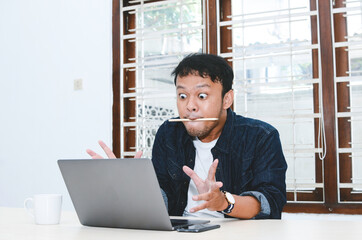 Young Asian man shocked and wow what he see in the laptop.