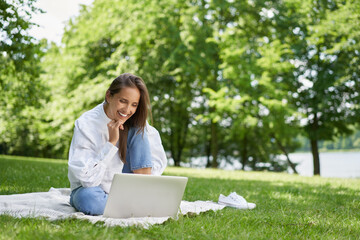Happy young woman using laptop in the park