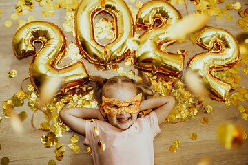 Cheerful Baby girl in mask with numbers 2022 rejoices at the confetti flying from above