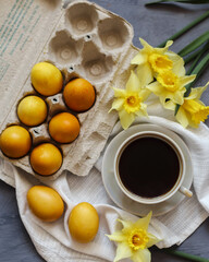 Cup of black tea and easter eggs on grey background with yellow flowers.