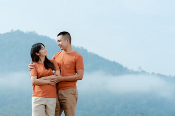 Portrait An Asian couple in identical brown shirts cuddling happily against a foggy and mountain backdrop.