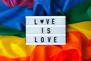 Rainbow flag with lightbox and text LOVE IS LOVE. Rainbow lgbtq flag made from silk material....