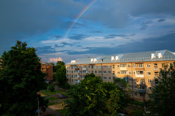 A rainbow in the blue evening sky with clouds over a Soviet-built multi-storey building in Russia.