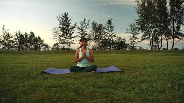 Woman sitting outdoor and doing yoga with headset on - concept of fitness people and music