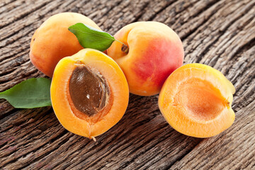 Ripe apricot fruits with slices and apricot leaves on a old wooden table.