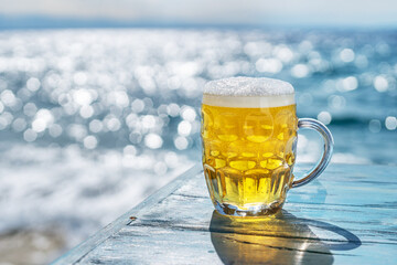 Chilled beer mug on the blue wooden table. Blurred sea is at the background.