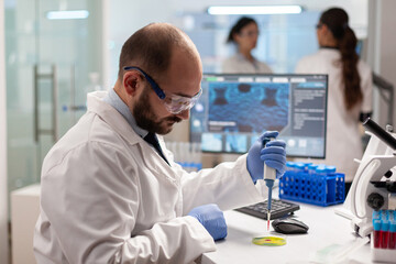 Biochemistry health care scientist testing blood sample using micropipette on petri dish. Team of...