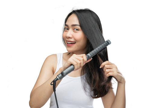 a smiling woman wearing underdress uses a hair straightener to straighten it on a gray background