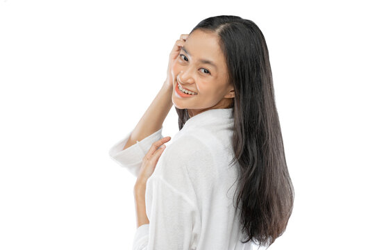 Beautiful woman with long hair standing sideways looking over her shoulder at the camera with smile against gray background