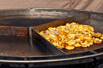 Roast potatoes in a large pan. Delicious food at the festival. Field kitchen at the hearth.