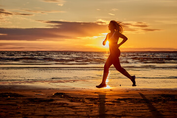 Fototapeta na wymiar Active lady runs near seaside on sand during sunset.