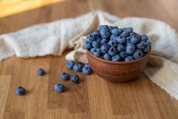Blueberries in clay bowl next to beige towel on a wooden background