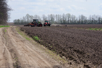 Fototapeta premium two red tractors, work in the field on a large tractor, harvesting, farming. two red tractors in a field in summer during an agricultural exhibition. Ukraine, Kiev region