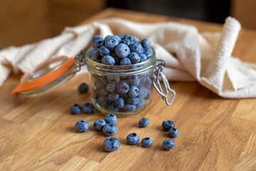 Blueberries in glass jar with beige towel on wooden table 